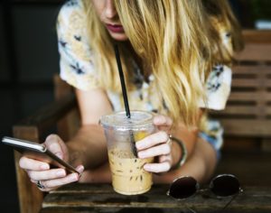 girl on her phone holding a cup of iced coffee